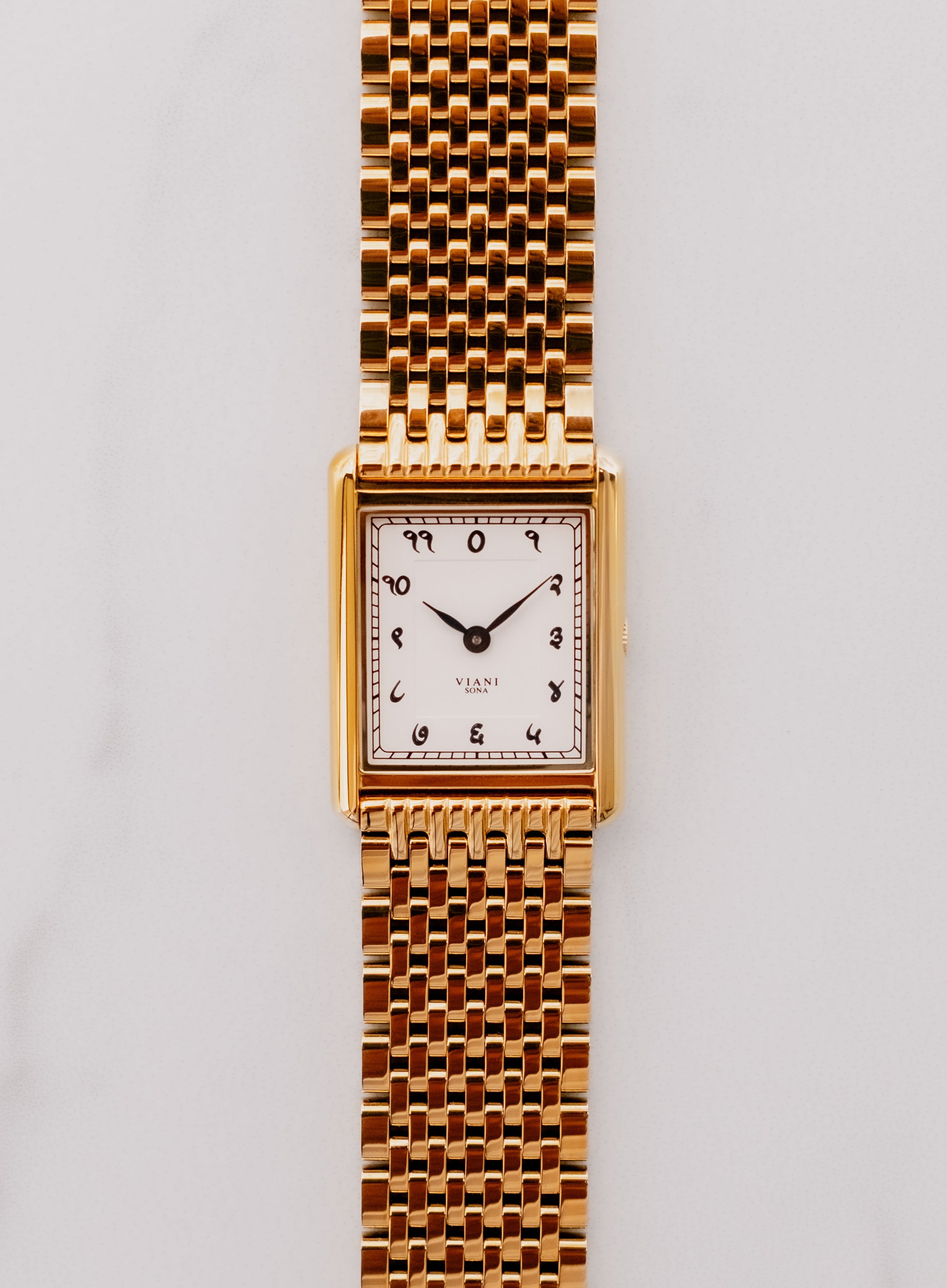 Gold wristwatch with a white face on a light gray background